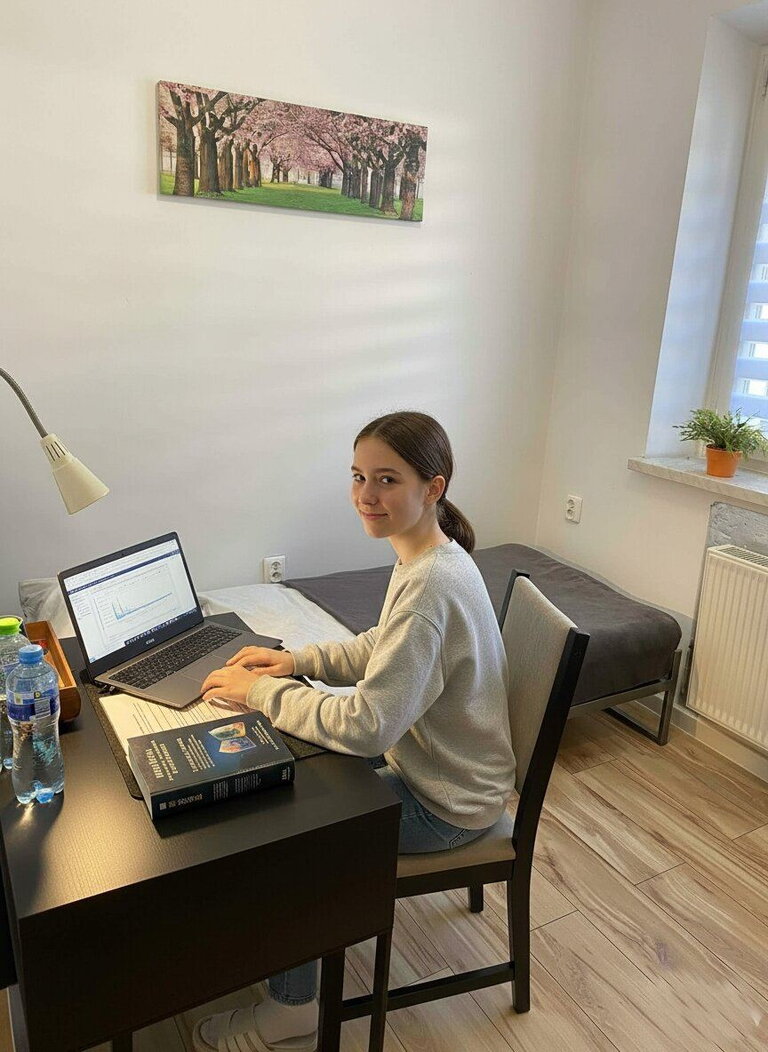 Smiling student girl studying at a desk with a laptop and books in a bright single room Smiling student girl studying at a desk with a laptop and books in a bright single room