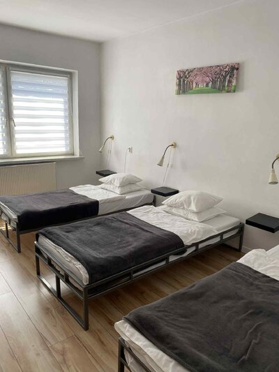 Jasny, minimalistyczny pokój z trzema pojedynczymi łóżkami, białymi ścianami, drewnianą podłogą i obrazem maków nad łóżkami. Jasny, minimalistyczny pokój z trzema pojedynczymi łóżkami, białymi ścianami, drewnianą podłogą i obrazem maków nad łóżkami.
