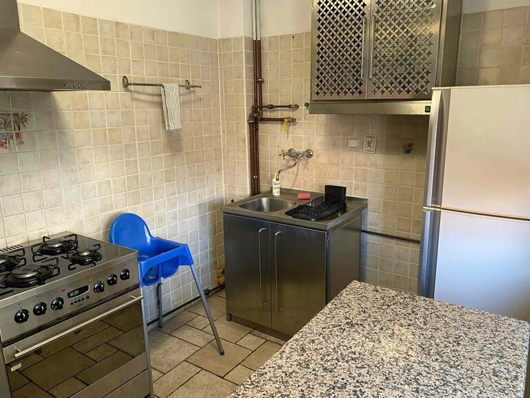 Kitchen with beige tiles, sink, gas cooker and fridge.