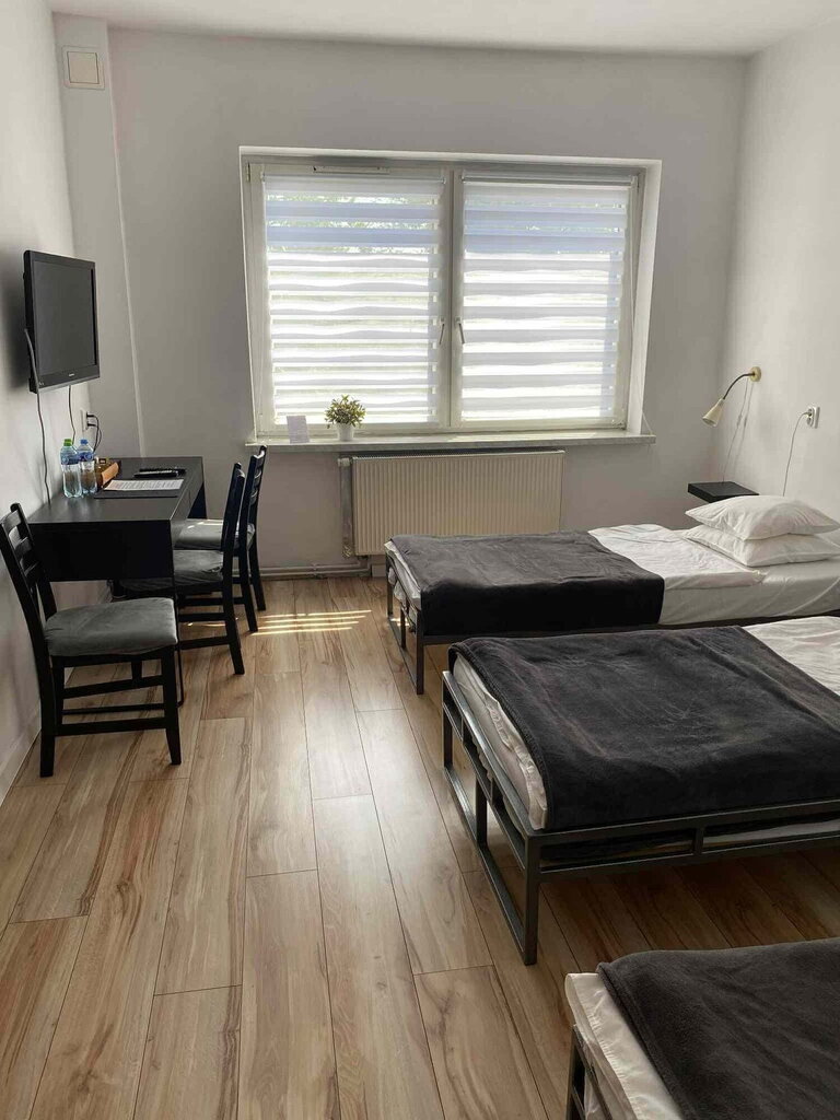 Bright triple room with three beds, desk, TV and window with blinds.