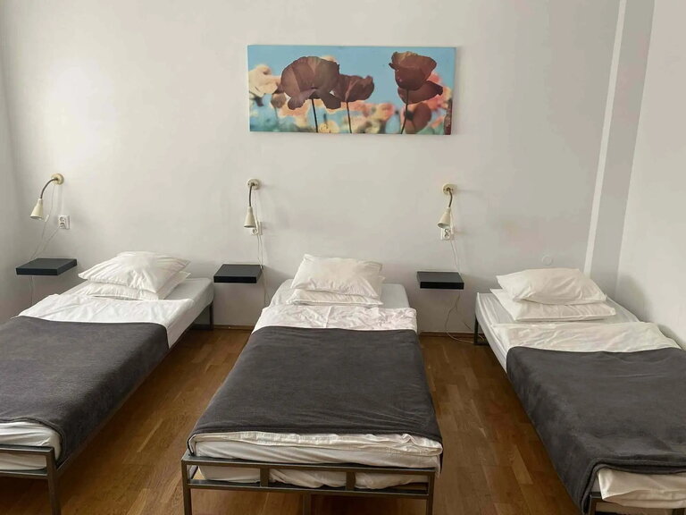 Bright, minimalist room with three beds, white walls and a poppy painting.