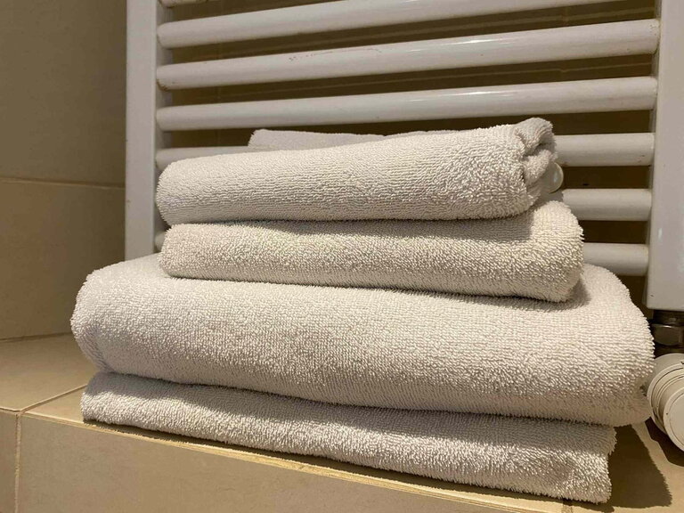 Asciugamani bianchi piegati impilati su piastrelle accanto a un termosifone del bagno