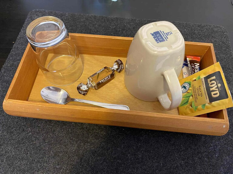 Kit di benvenuto con tazza, tĂš, caffĂš e dolcetti su un letto alla pensione Nest PoznaĆ.