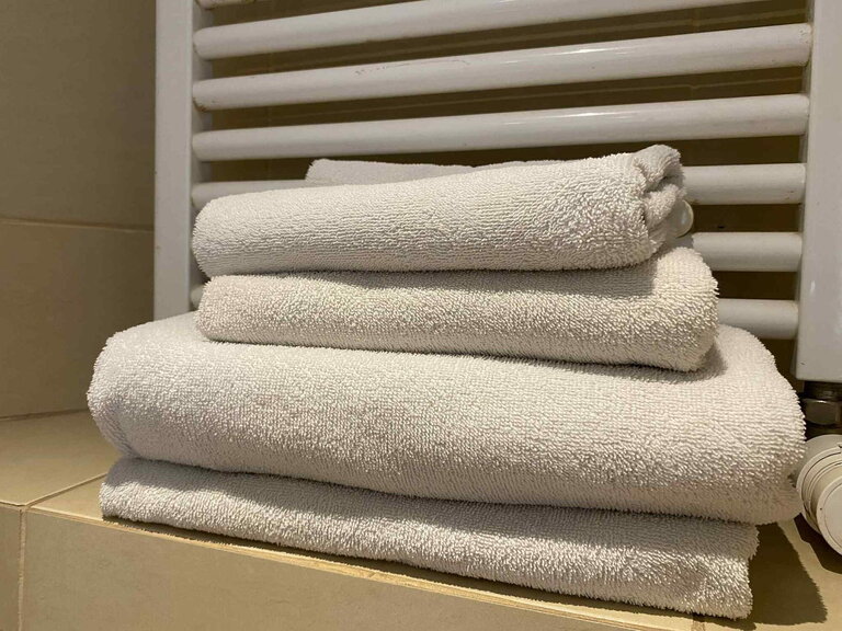 Folded white towels stacked on tiles next to a bathroom radiator